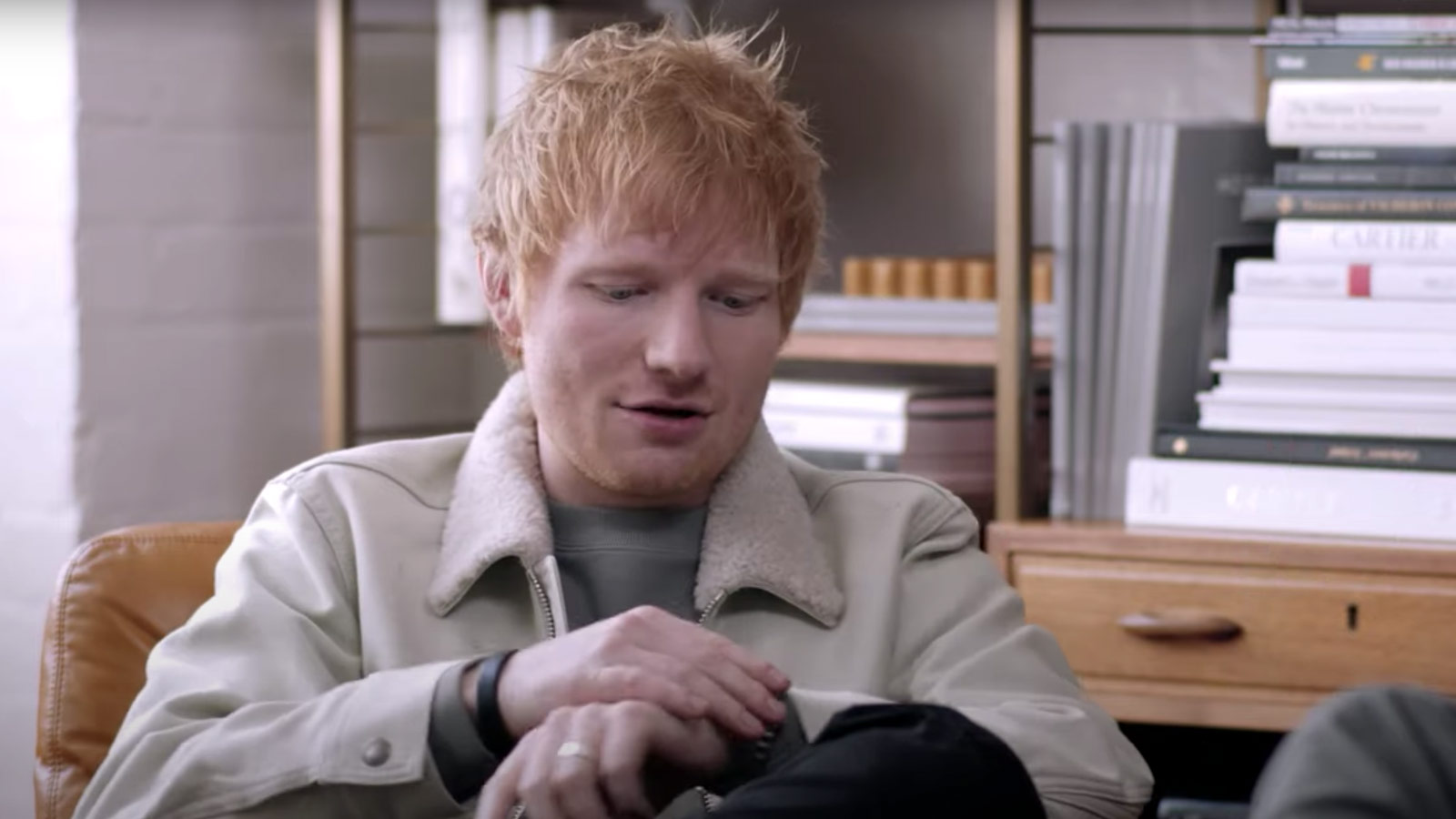 Ed Sheeran prater og ser ned på håndleddet sitt.